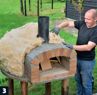 Isoleringen av mineralull läggs nu över murad pizzaugn Isoleringen av mineralull läggs nu över murad pizzaugn